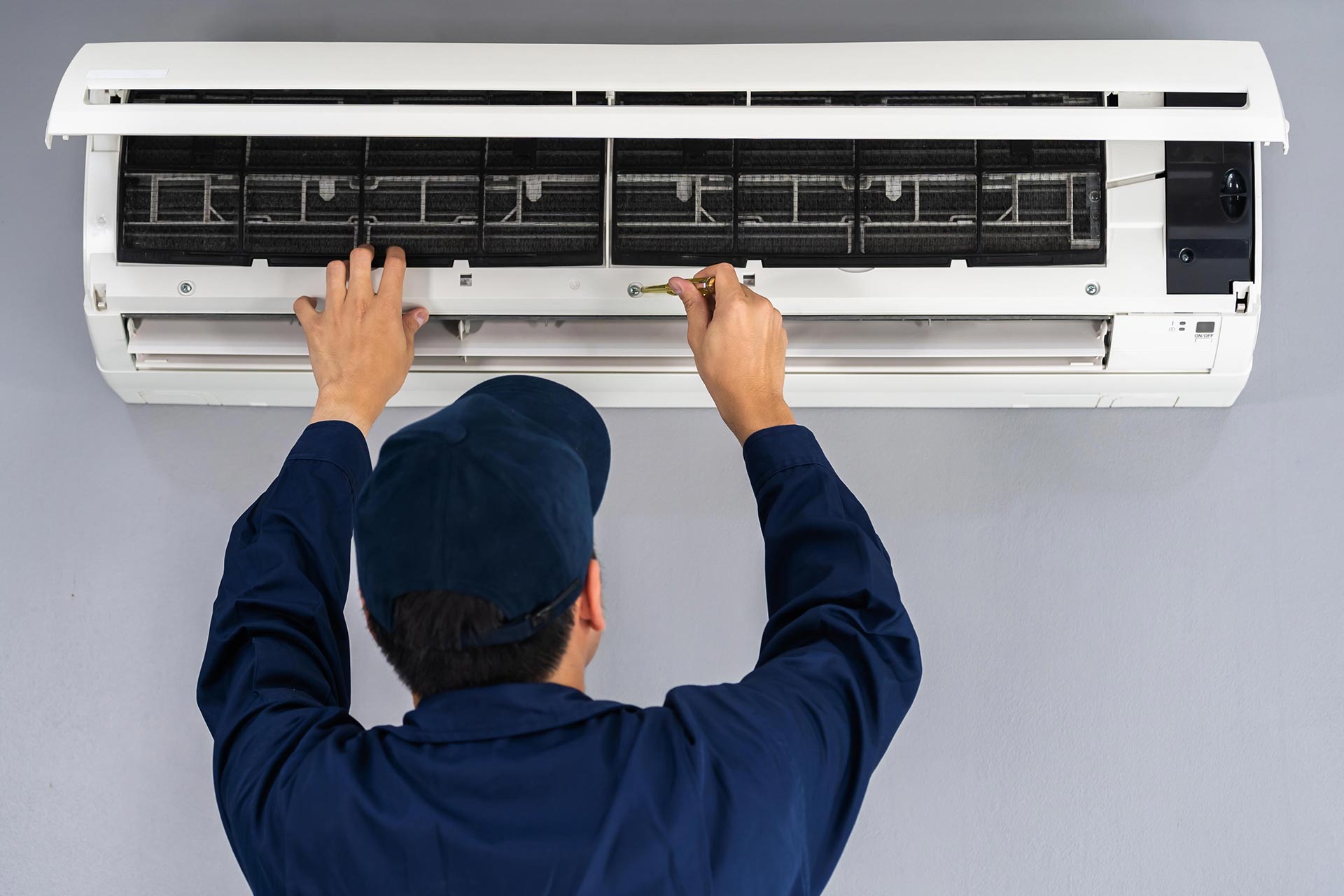 Tecnico in uniforme blu esegue la manutenzione di un condizionatore split, pulendo i filtri interni. Offriamo servizi di pompe di calore Torino.
