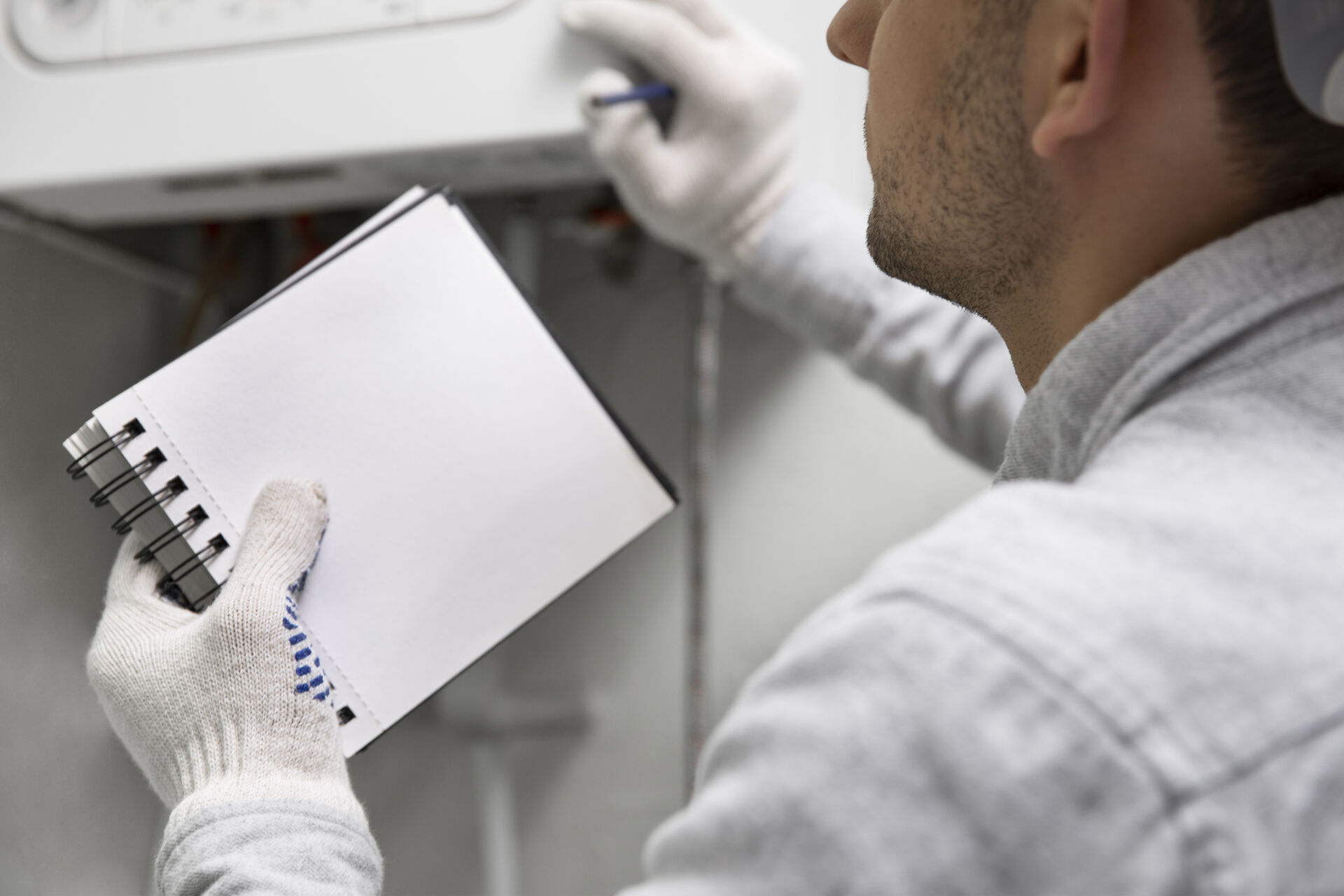 Tecnico con guanti bianchi e quaderno annota dettagli durante l'installazione o manutenzione di un impianto, forse una pompa di calore, a Torino.