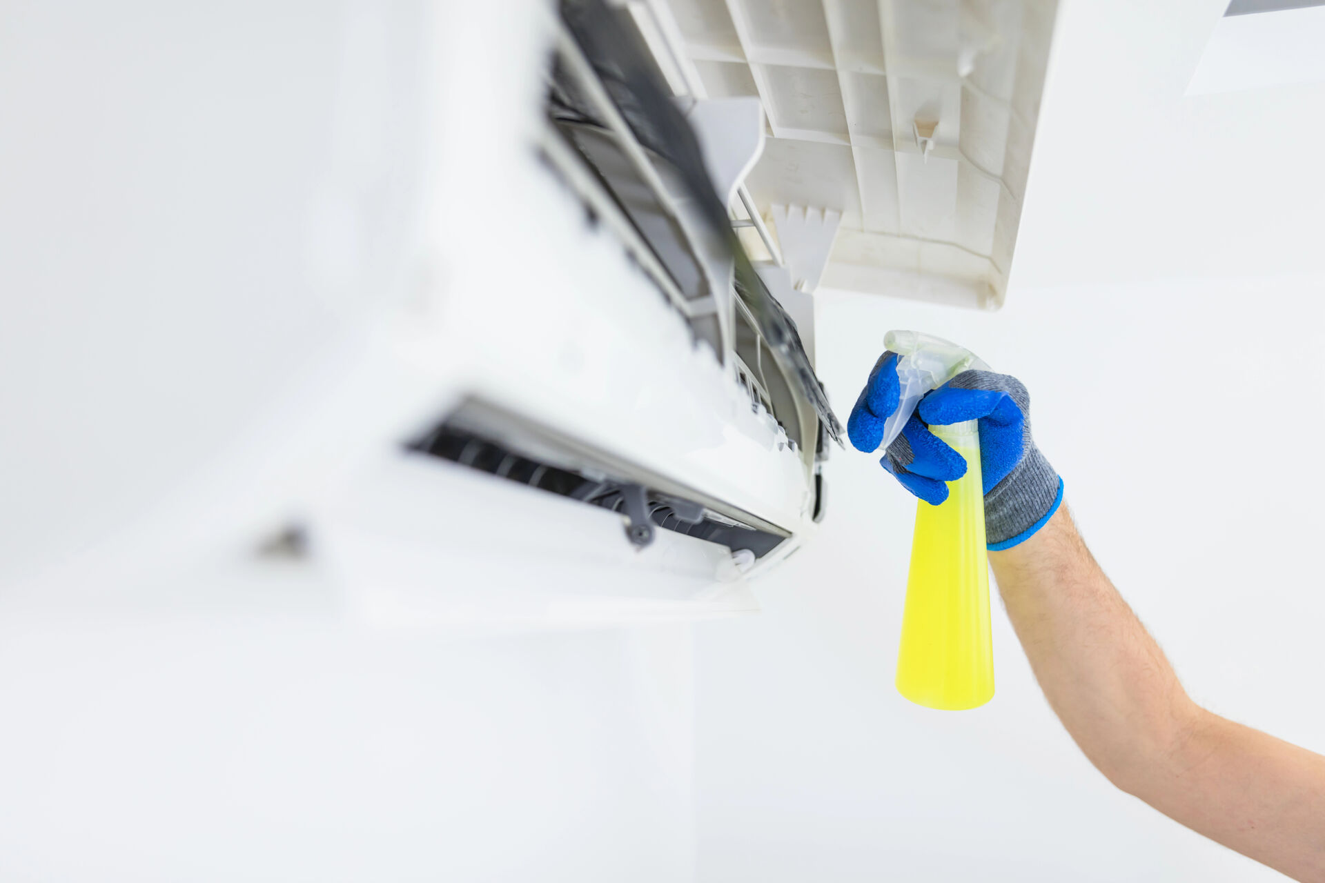 Mano con guanto blu che spruzza prodotto detergente all'interno di un climatizzatore aperto, per pulizia e manutenzione.